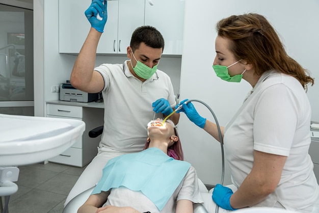 Patient is lying in dentistry where she is being treated by male somatologist female assistant