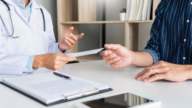 Пациент внимательно прислушивается к врачу-мужчине, объясняющему симптомы пациента или задающему вопрос, когда они вместе обсуждают документы на консультации