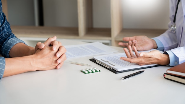 Patient listening intently to a male doctor explaining patient symptoms or asking a question as they discuss paperwork together in a consultation