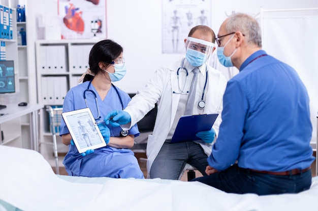 Patient looking at radiography of his skeleton during consultation with doctor in hospital wearing protection against covid-19