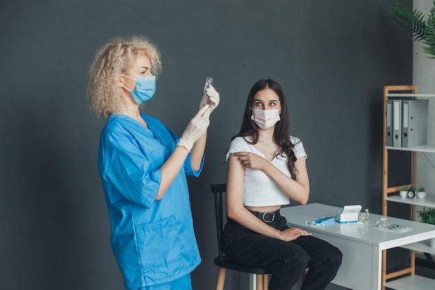 Photo patient in medical face mask looking at needle of the vaccine syringe held by the doctor in the hospital coronavirus vaccination pandemic prevention virus epidemic disease