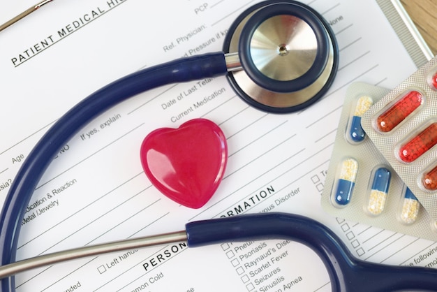 Patiënt medische geschiedenis formulier met rood hart stethoscoop en pillen packs close-up