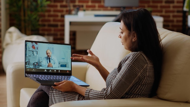 Patiënt op de bank die tijdens een online videocall een behandelplan ontvangt van een arts