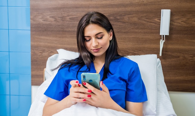 Patiënt praten op mobiele telefoon in ziekenhuisbed. Jonge blanke vrouw.