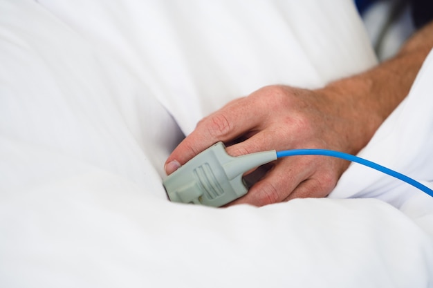 Patient's Hand with Pulse Oximeter on Finger for Monitoring in modern Hospital.