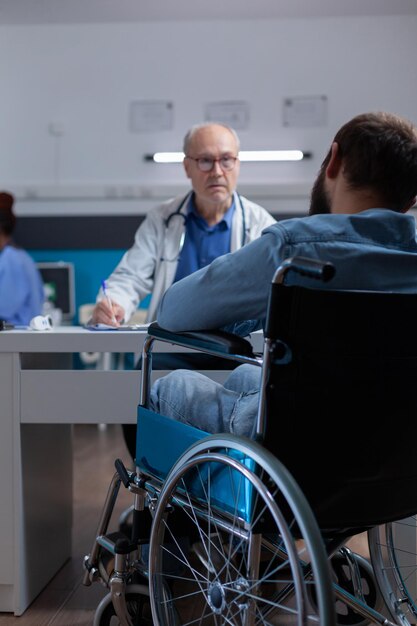 Patient sitting in wheelchair meeting with specialist at
checkup visit to cure illness. man with physical disability talking
to medic about healthcare and treatment against disease in
office.