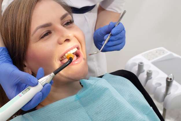 The patient at the stamotologa in a chair, a girl with a snow-white smile, she makes a seal and light a special lamp. The concept of dental treatment, or oral health .