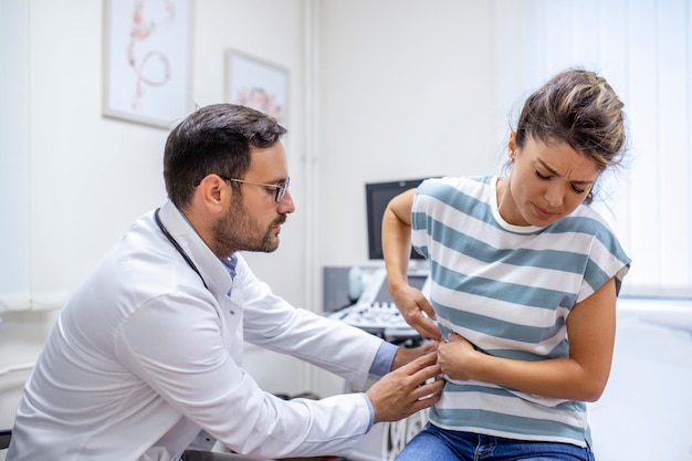 Patient telling physician about her pain and health problems during visit to hospital Young woman complaining about back or kidney ache while sitting on examination bed at the doctors office