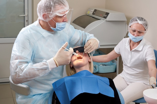 Patient visiting a dental office. Adult woman sitting in chair. Dentist hands in rubber protective gloves.