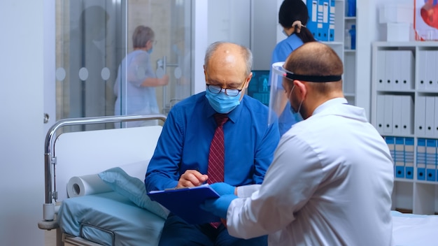 보호 마스크를 착용하고 퇴원 양식에 서명하는 환자. 글로벌 전염병 동안 COVID-19 의료 의료 상담. 개인 현대 건강 클리닉 또는 병원, 의료 의학 치료