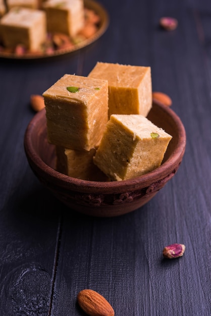 Patisa of Soan Papdi is een populair Indiaas flakey en knapperig dessert in de vorm van een kubus. Geserveerd met amandelen en pistache in een bord op een humeurige achtergrond. Selectieve focus