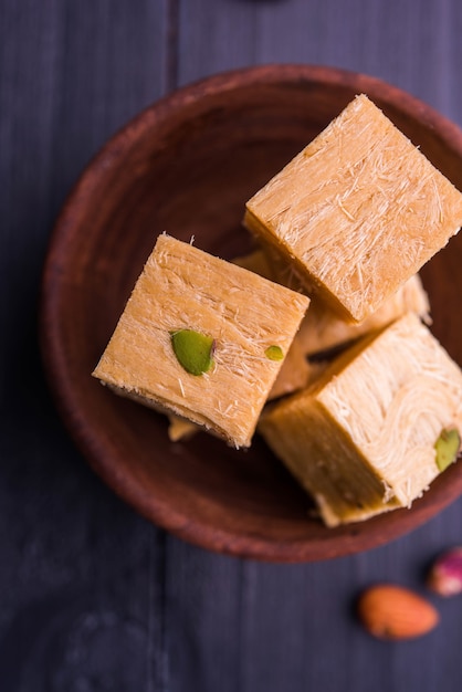 Foto patisa of soan papdi is een populair indiaas flakey en knapperig dessert in de vorm van een kubus. geserveerd met amandelen en pistache in een bord op een humeurige achtergrond. selectieve focus