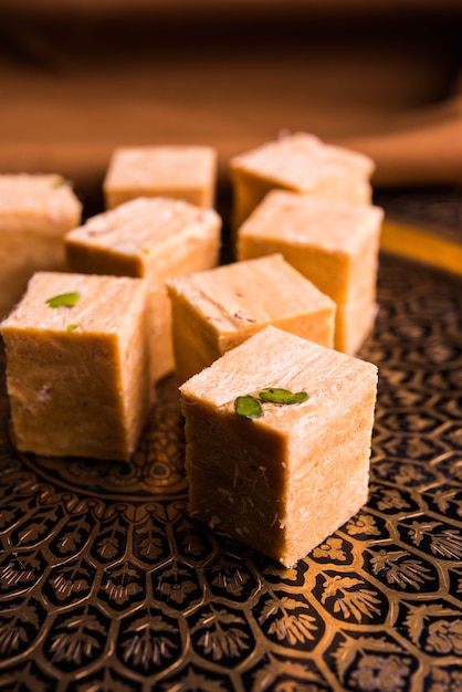 Photo patisa or soan papdi is a popular indian cube shape flakey and crispy dessert. served with almonds and pistachio in a plate over moody background. selective focus