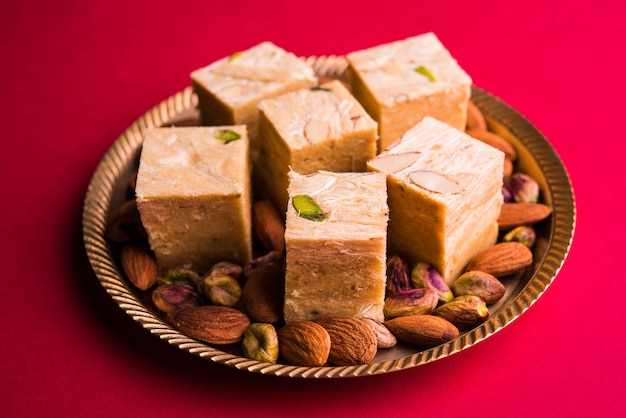 Patisa or Soan Papdi is a popular Indian cube shape flakey and crispy dessert. Served with almonds and pistachio in a plate over moody background. Selective focus
