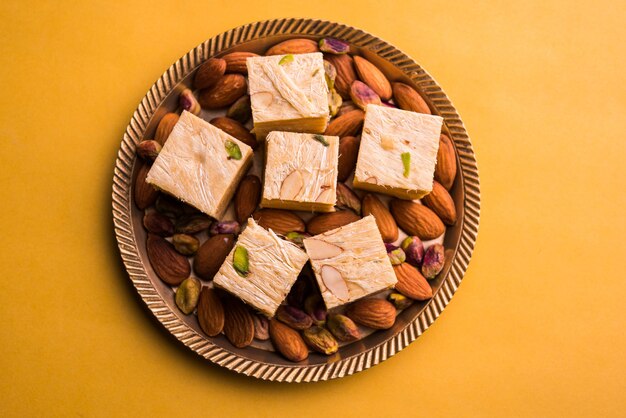 Patisa or Soan Papdi is a popular Indian cube shape flakey and crispy dessert. Served with almonds and pistachio in a plate over moody background. Selective focus