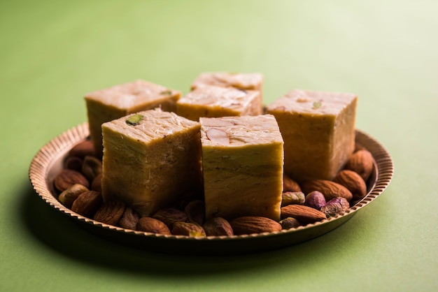 Foto patisa o soan papdi è un popolare dolce indiano a forma di cubo e croccante. servito con mandorle e pistacchi in un piatto su sfondo lunatico. messa a fuoco selettiva