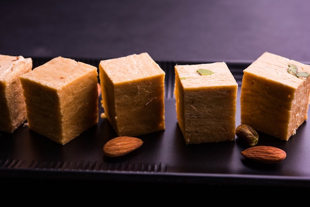 Патиса или Соан Папди - популярный в Индии хрустящий десерт в форме куба. Подается с миндалем и фисташками в тарелке на мрачном фоне. Выборочный фокус