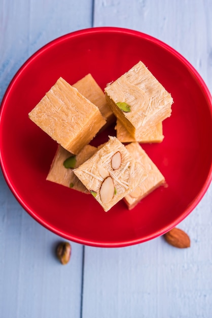 Patisa or Soan Papdi is a popular Indian cube shape flakey and crispy dessert. Served with almonds and pistachio in a plate over moody background. Selective focus