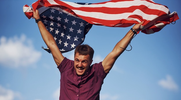 Photo patriotic happy man waving american flag against cloudy blue sky.