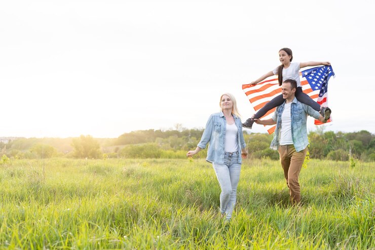 Patriotic holiday. Happy family, parents and daughters children girl with American flag outdoors. USA celebrate 4th of July.