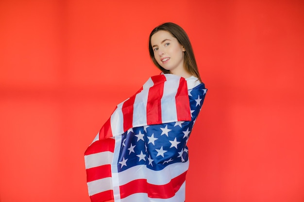 愛国的な休日赤い背景のアメリカの国旗を持つ幸せな若い女性は7月4日を祝う