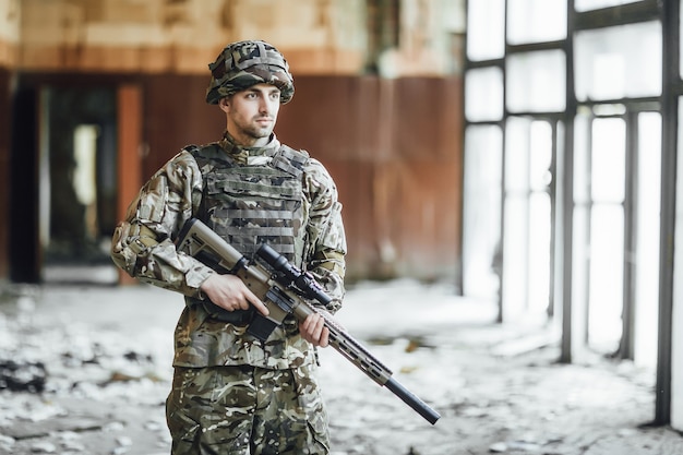 Patrols the territory. young soldier in the military stands at the window of the collapsed building