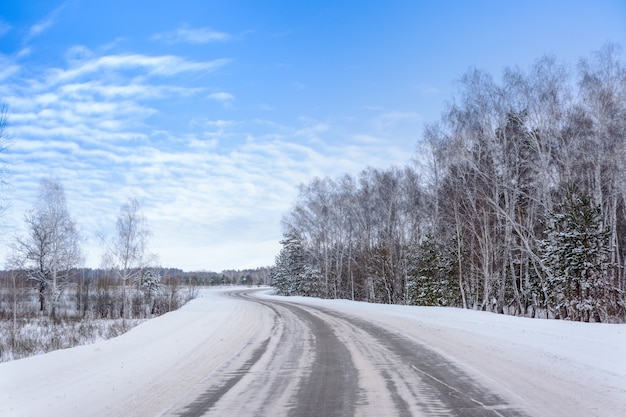 Patronen op de wintersnelweg in de vorm van vier rechte lijnen. Besneeuwde weg op de achtergrond van besneeuwd bos. Winterlandschap.