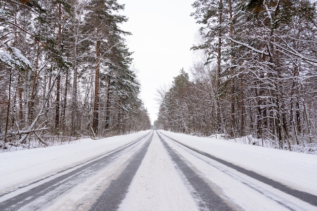 Patronen op de wintersnelweg in de vorm van vier rechte lijnen. Besneeuwde weg op de achtergrond van besneeuwd bos. Winterlandschap.