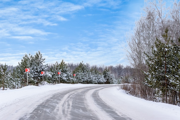 Patronen op de wintersnelweg in de vorm van vier rechte lijnen. Besneeuwde weg op de achtergrond van besneeuwd bos. Winterlandschap.