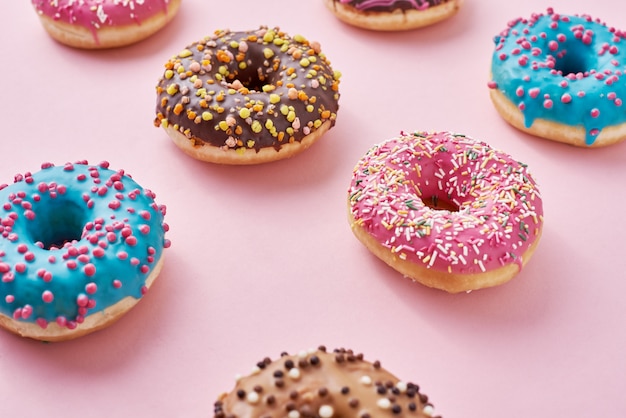 Patroon met verschillende soorten kleurrijke donats versierd hagelslag en suikerglazuur op pastel roze, bovenaanzicht plat lag