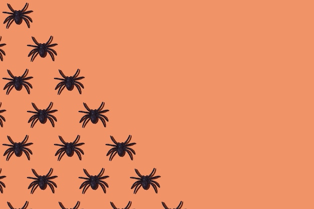 Foto patroon van glanzende plastic spinnen als decoratie voor halloween aan de linkerkant op oranje achtergrond concept van terreur fobie angst viering arachnofobie dag van de doden afweermiddel en speelgoed