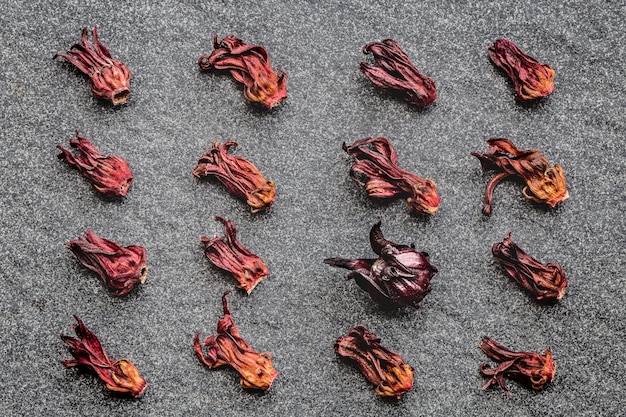 Foto patroon van hibiscus gedroogde bloemen (roselle, karkade) en één vers op zwarte stenen achtergrond.