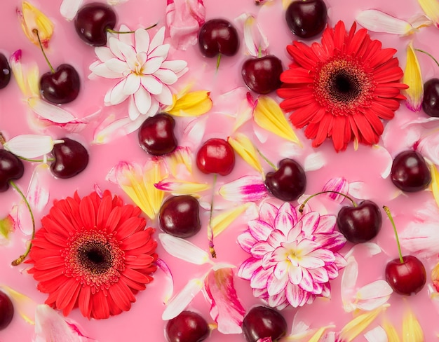 Patroon van kersen, rode herbera's en bloemblaadjes op rozenwater, plat leggen