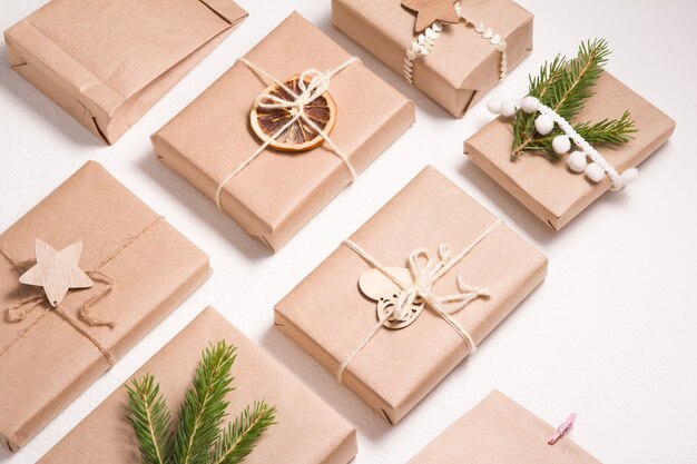 Patroon van verschillende kerstcadeaudozen in eco-vriendelijke stijl op een witte achtergrond, decor van houten kerstboomspeelgoed, gedroogde sinaasappel- en sparrentak