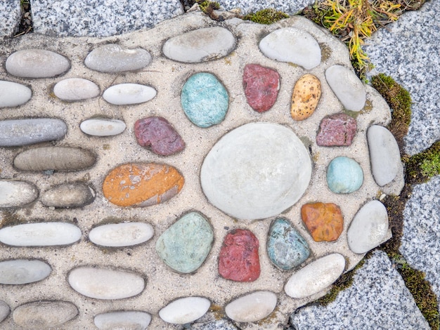 Patroon van zeesteenen in cement Grondbedekking in het park achtergrond met hobbels achtergrond van strandkiezels en beton Ongebruikelijk ontwerp Verschillende kleuren stenen