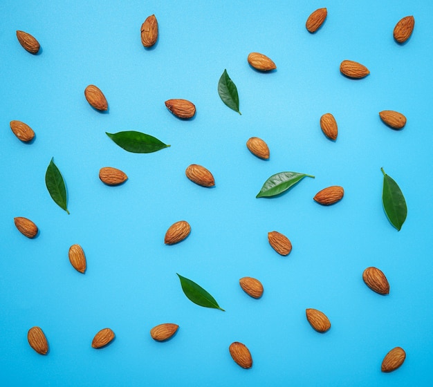 Pattern of almonds nuts arrange on blue with green leaf