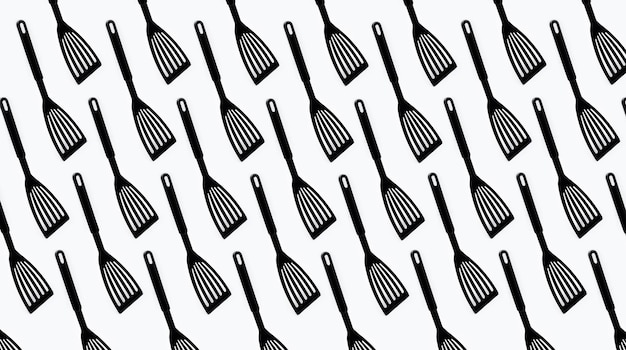 Pattern of black plastic turner spatula on white background