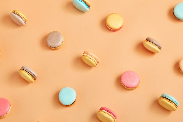 a pattern of colorful french cookies macarons on yellow peach background