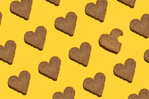 Pattern made with bread in heart form on yellow background as backdrop or texture Bright food wallpaper Top view Flat lay