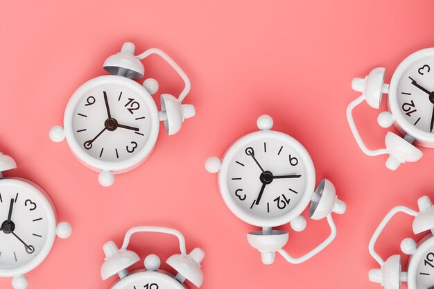 A pattern of many white classic alarm clocks in the form of a pattern on a pink background. Top view with a copy of the space, flat lay.