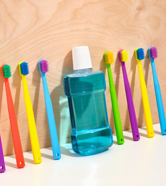 Photo a pattern of multicolored toothbrushes and blue mouthwash near a wooden wall concept of mouth hygiene hygiene