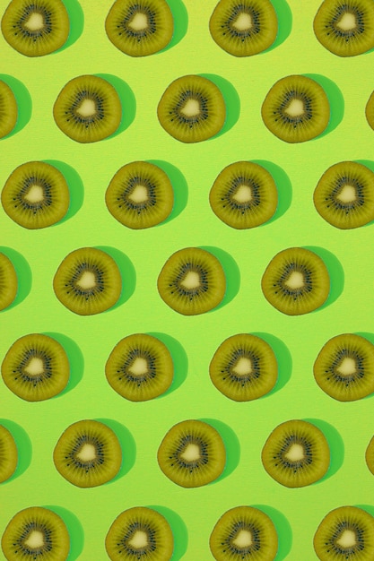 写真 キウイのパターン。緑の背景にスライスしたキウイの上面図。最小限のフラットレイコンセプト。印刷