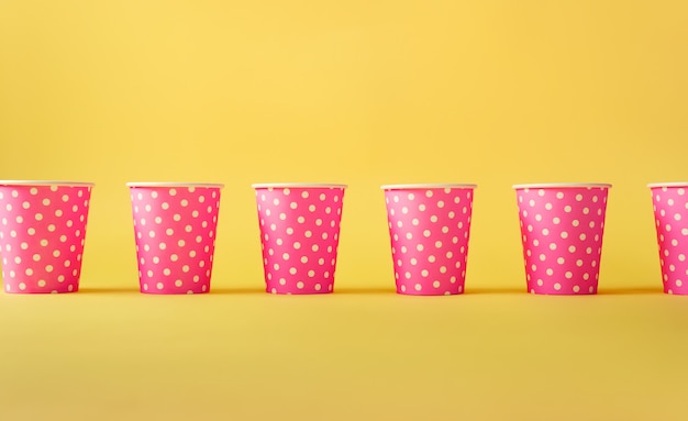 Photo pattern of pink polka dot paper cups on yellow background.