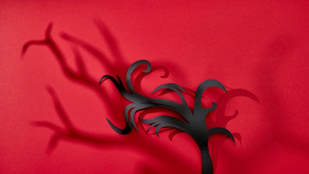 影のパターンとテキスト用のスペースのある赤い背景の上の手漉き紙の黒い枝。ハロウィンカード。フラットレイ