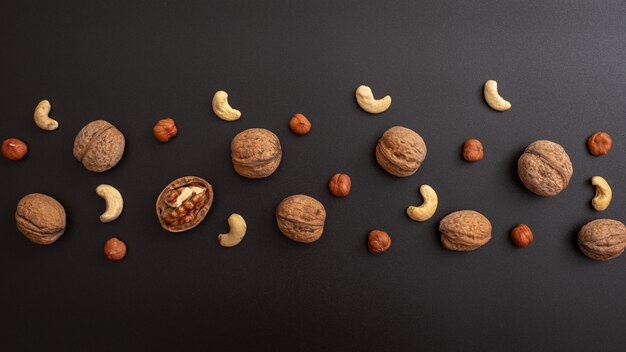 Pattern shelled walnut, hazelnut and cashews on black table.