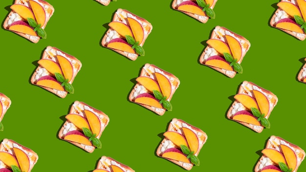 Pattern of toasted bread with peach and basil on green background