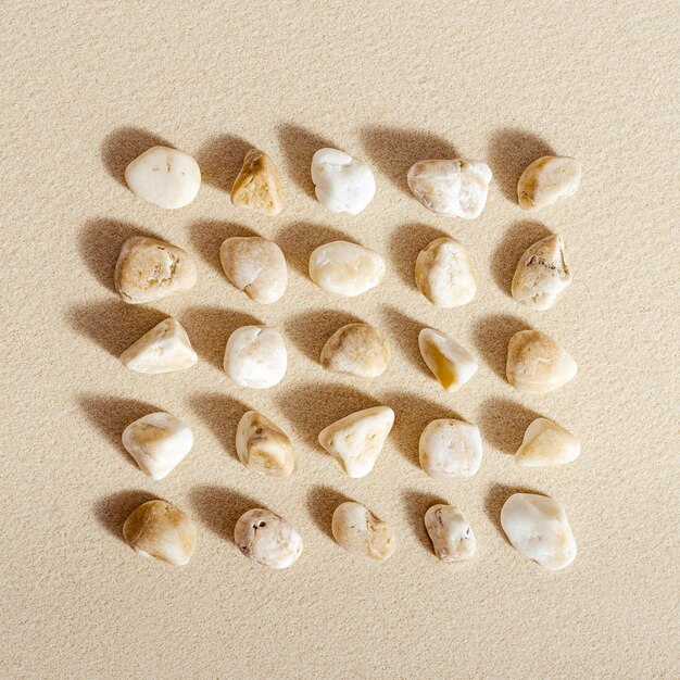 Pattern with close up pebble sea stones on sand texture. Square composition from natural stone neutral natural tones. Minimal style background, concept of calm, peace, meditation. View from above.