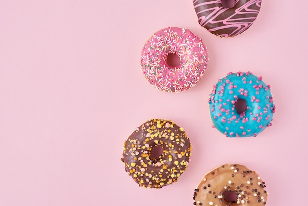 Pattern with different types of colorful donats decorated sprinkles and icing on pastel pink background, top view flat lay