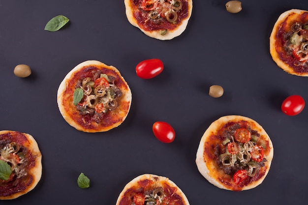 Pattern con mini pizza fatta in casa, pomodorini e olive verdi su fondo nero