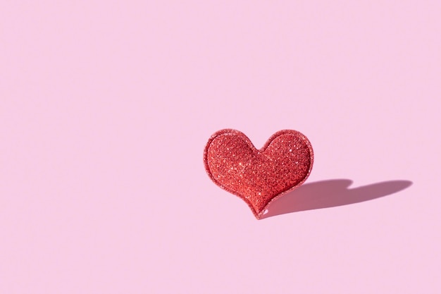 Узор с красным блеском в форме сердца на розовом фоне с жесткой тенью Скопируйте пространство День Святого Валентина минималистичный символ любви
